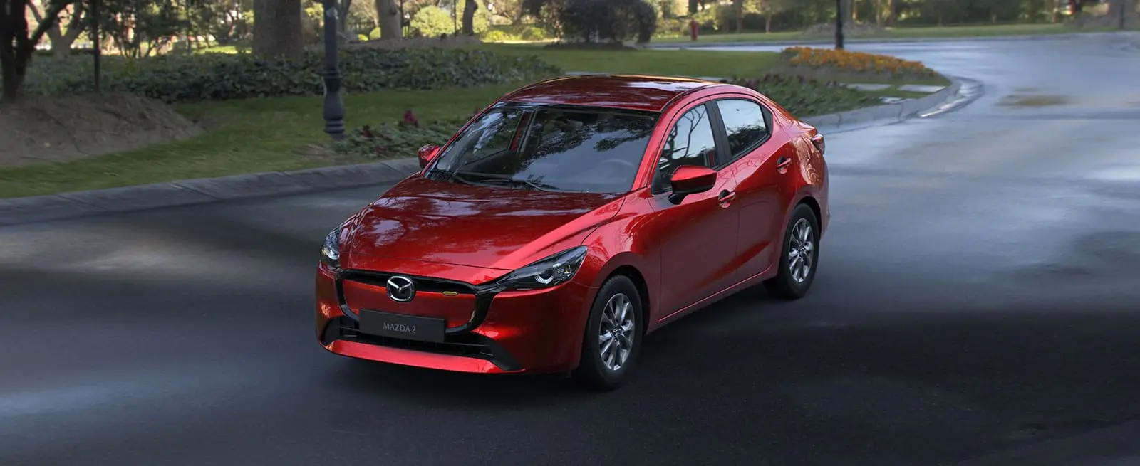 Mazda 2 Sedán color Rojo Diamante, vista frontal en parque